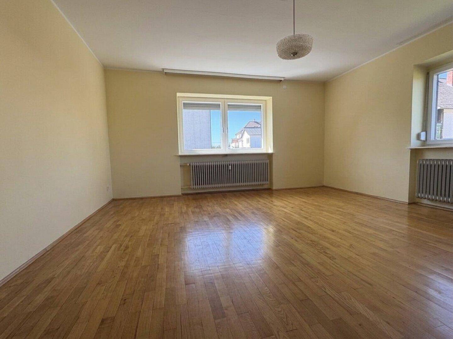 Geräumiges Zimmer mit Parkettboden und großen Fenstern, die viel Tageslicht in den Raum bringen.