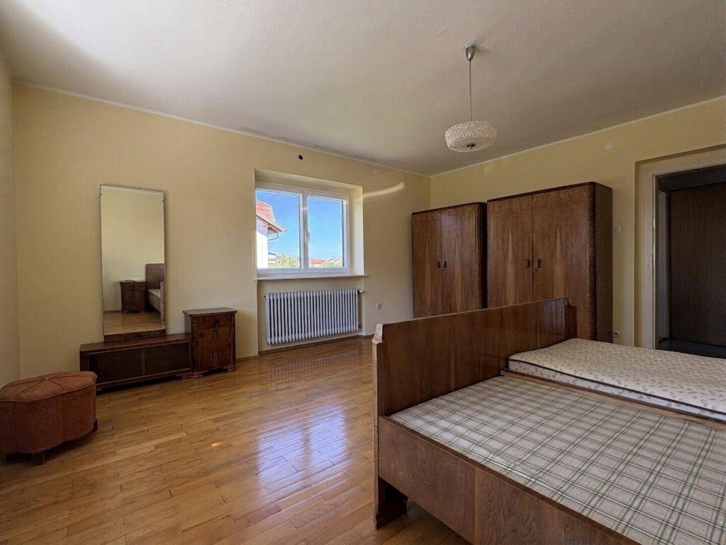 Schlafzimmer mit Parkettboden, Holzmöbeln und einem Fenster mit Blick nach draußen.