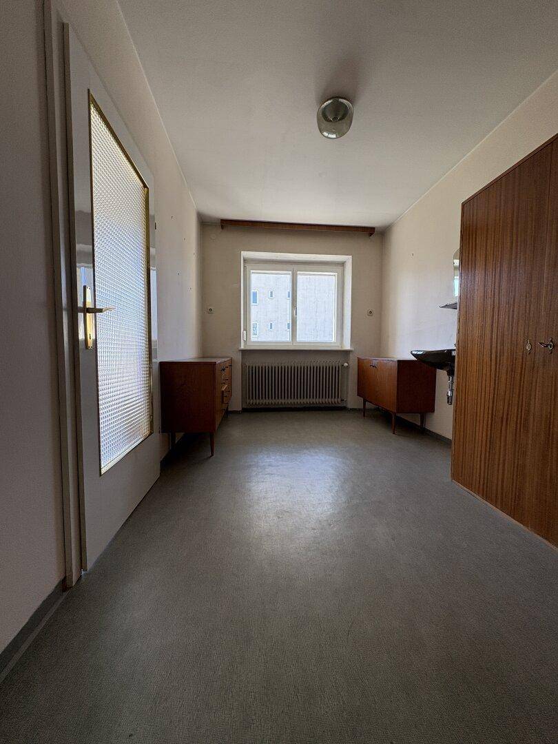 Kleiner Raum mit Linoleumboden, Fenster und einfachen Holzschränken, möglicherweise ein Abstellraum.