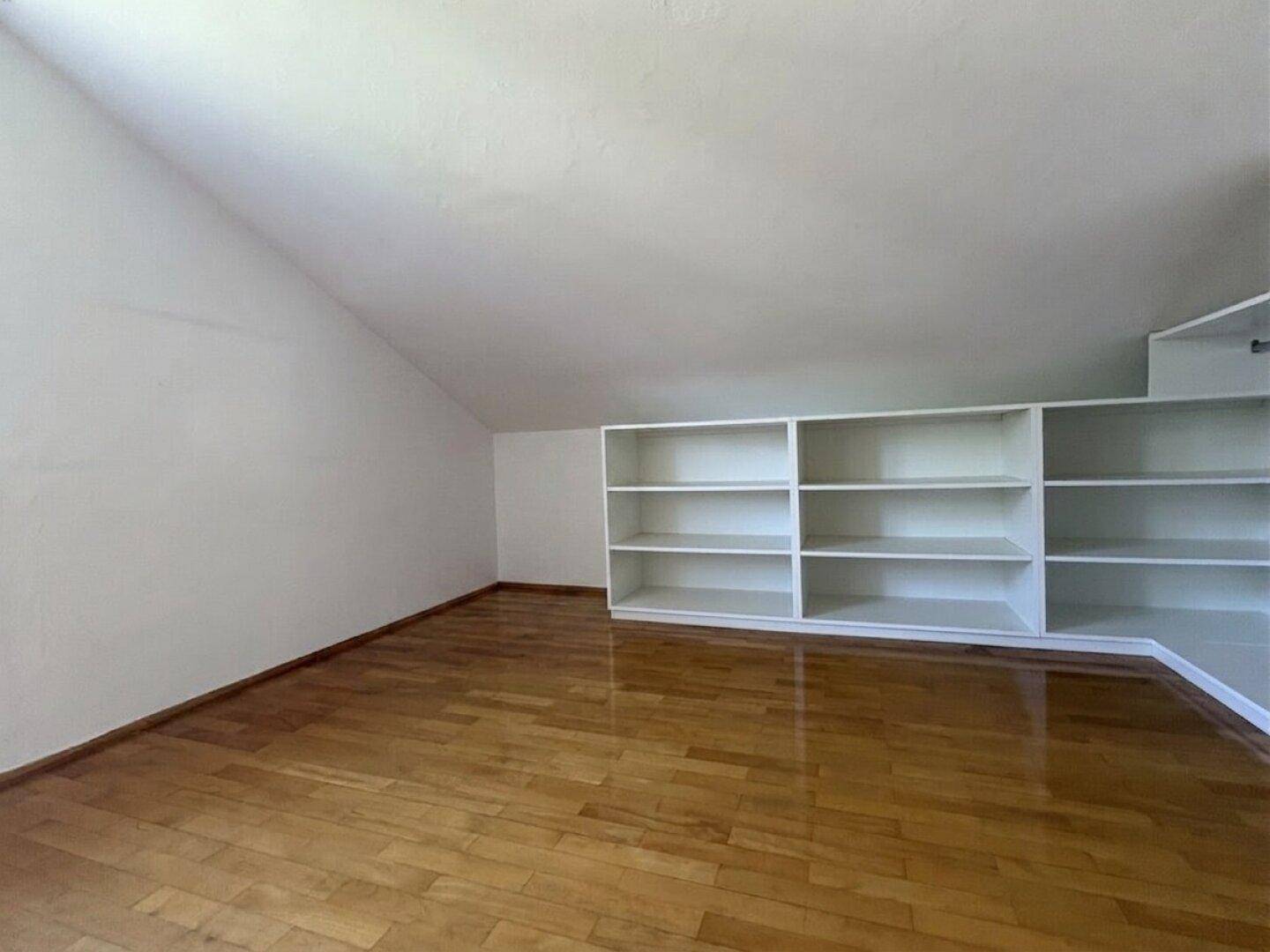 Heller Dachgeschossraum mit Holzboden, schrägen Wänden und integrierten Regalen für zusätzlichen Stauraum.