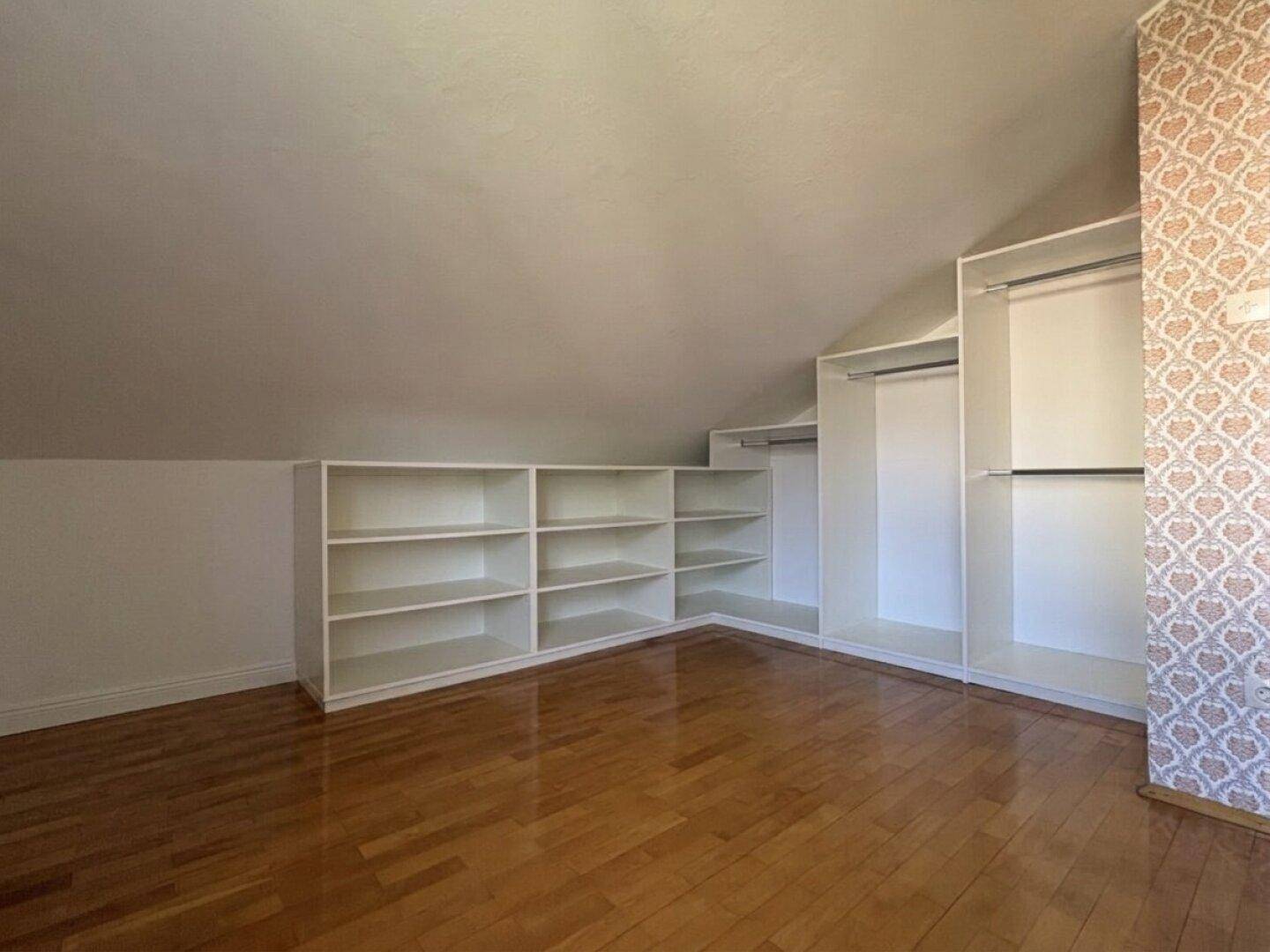 Dachgeschossraum mit Holzboden, schrägen Wänden und praktischen eingebauten Regalen für Stauraum.