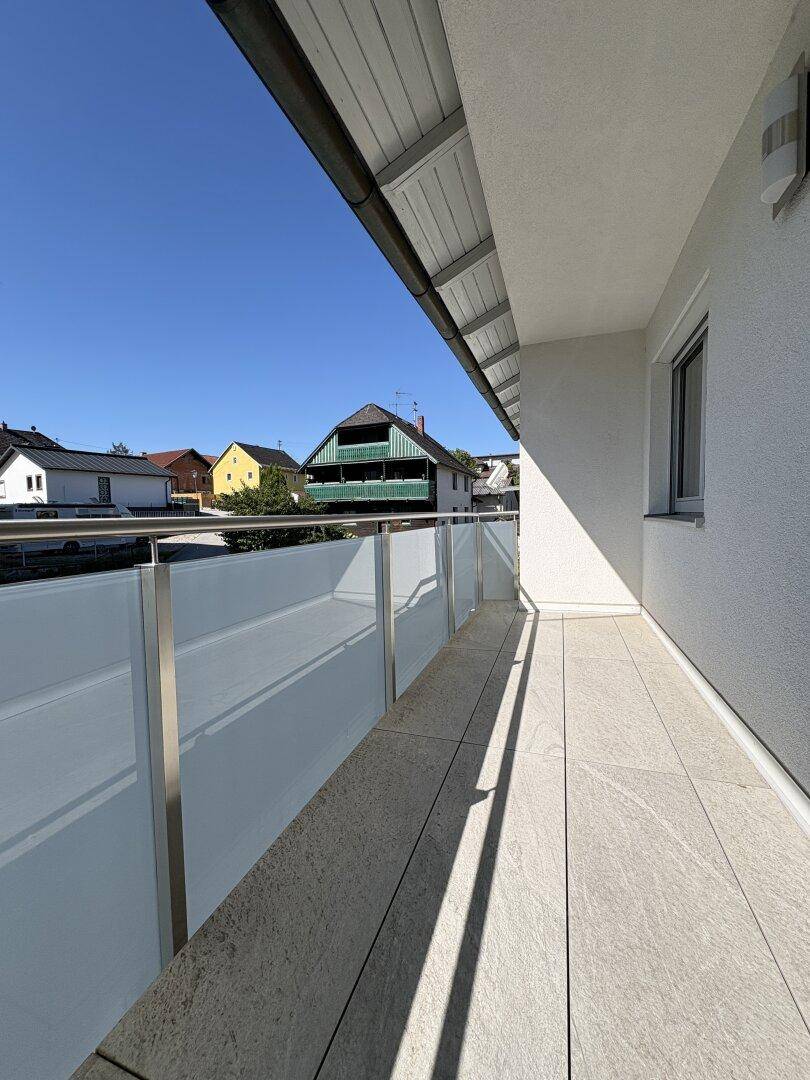 Langer Balkon mit Fliesenboden und Blick auf die Nachbarschaft unter blauem Himmel.