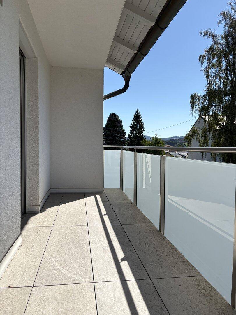 Sonniger Balkon mit modernen Glasgeländern und Blick auf die umliegende Landschaft.