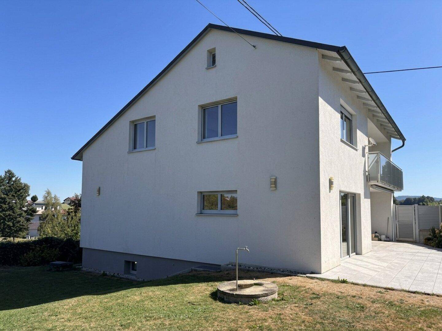 Freistehendes Einfamilienhaus mit weißer Fassade, Satteldach und einem gepflegten Gartenbereich.
