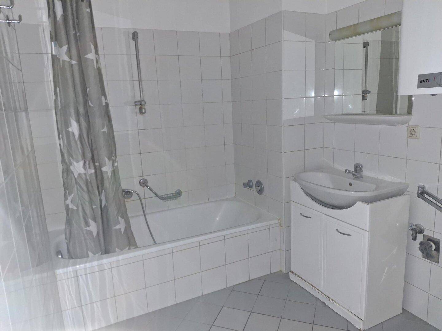 Gefliestes Badezimmer mit Badewanne, Waschbecken und Spiegel, in gutem Zustand.