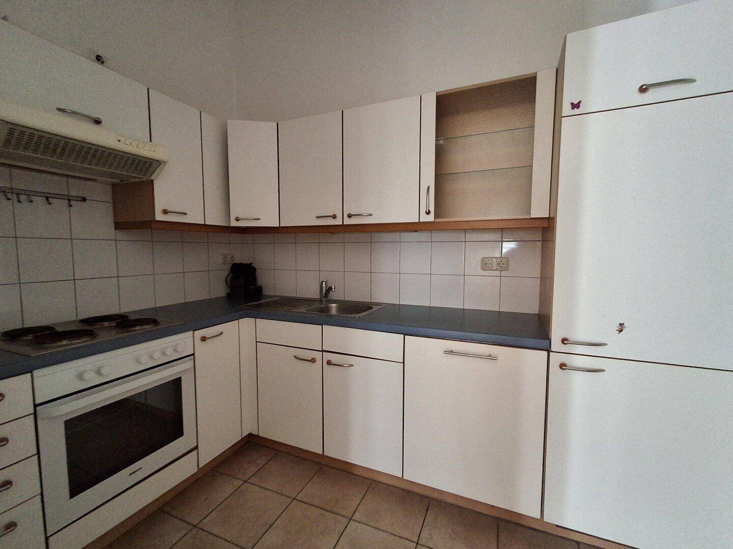 Funktionale Küche mit weißen Schränken, blauer Arbeitsplatte und Fliesenboden in Standardausstattung.
