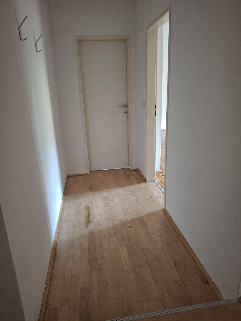 Heller Flur mit Holzfußboden und weiß gestrichenen Wänden, der zu weiteren Räumen führt.