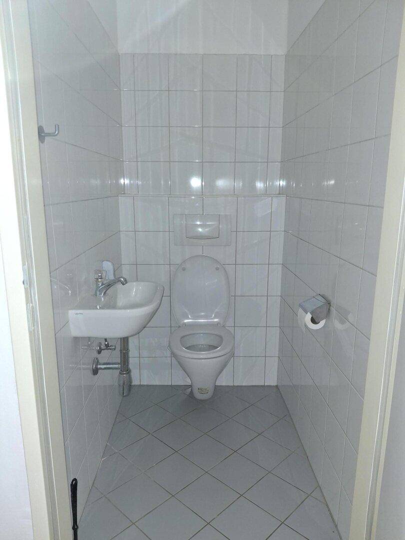 Kleines, gefliestes Gäste-WC mit Toilette und Handwaschbecken, hell und sauber.