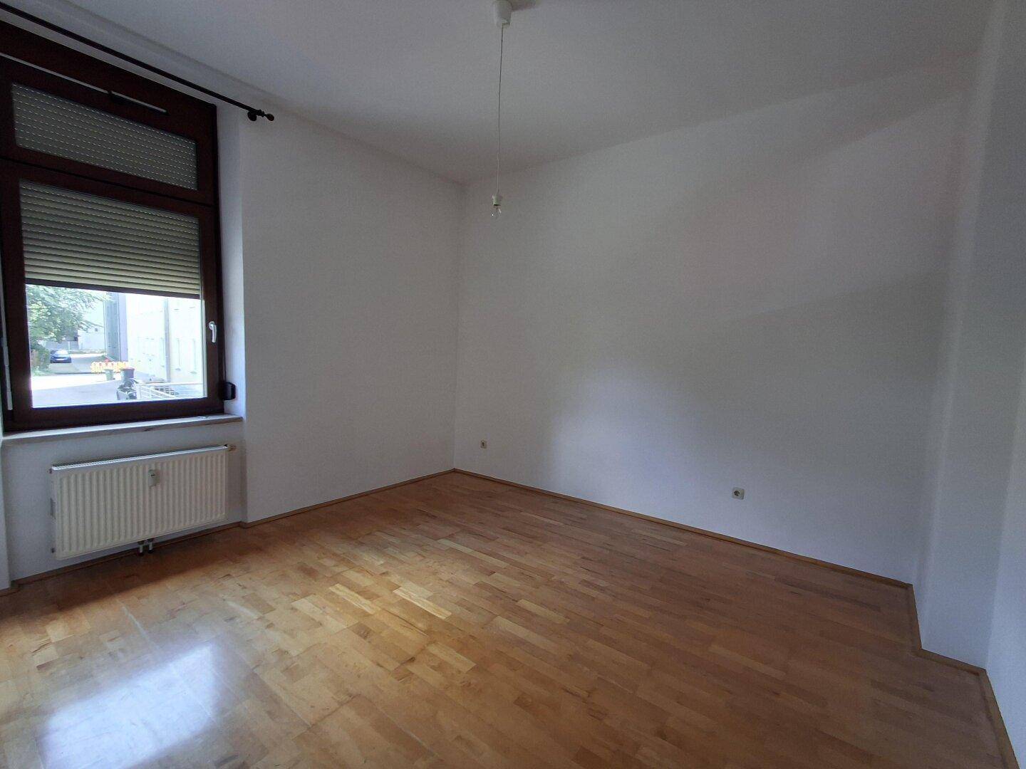 Leeres Zimmer mit Holzboden und einem Fenster, das viel Tageslicht hereinlässt.