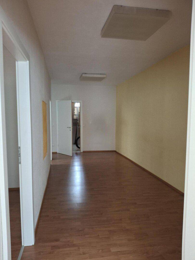 Langer Flur mit Laminatboden, hellen Wänden und mehreren Türen, der verschiedene Räume verbindet.