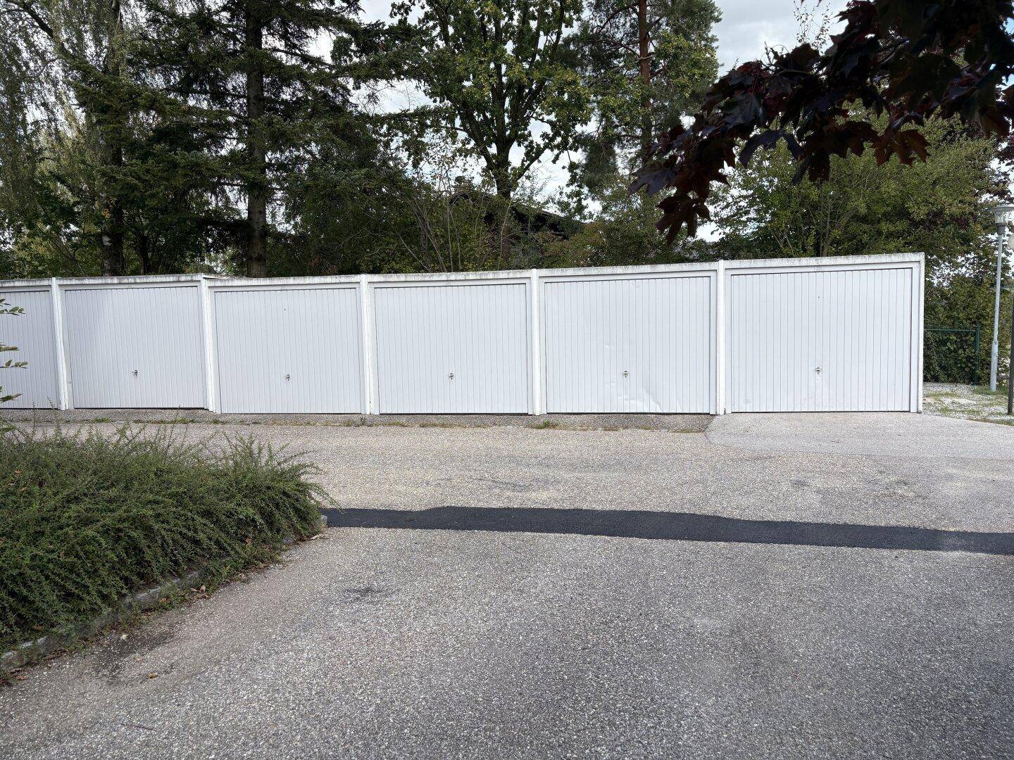 Reihe von Garagen mit weißen Toren und einer asphaltierten Zufahrt für Fahrzeuge.