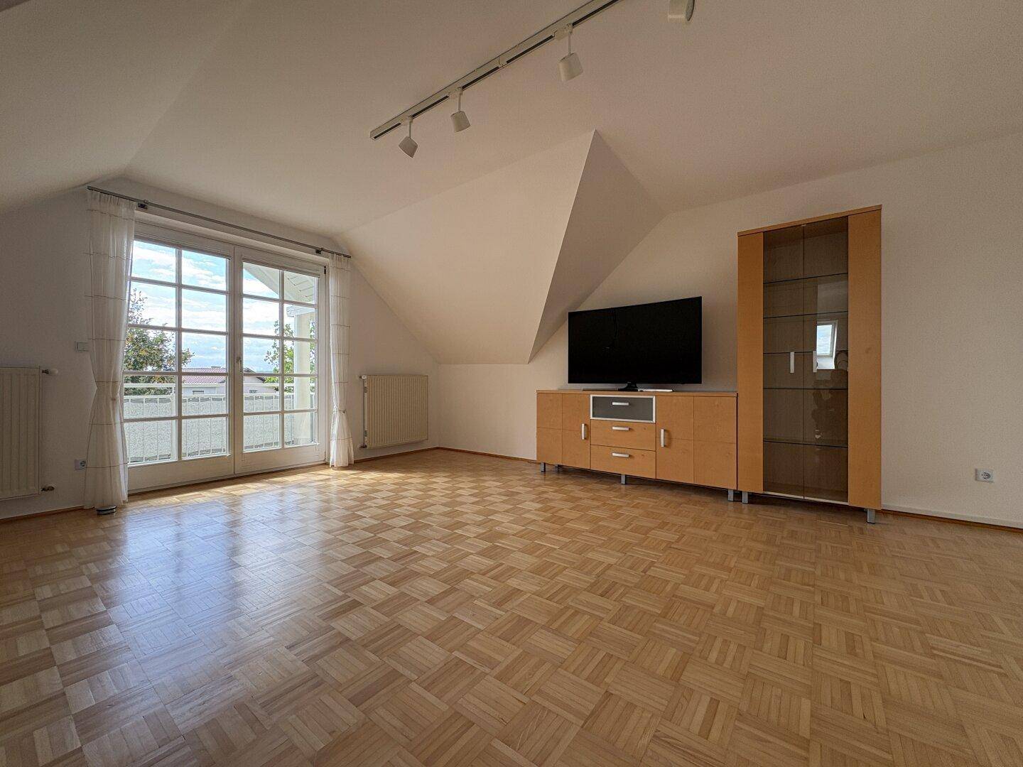 Geräumiges Wohnzimmer mit Parkettboden, Balkonzugang und Blick ins Grüne.