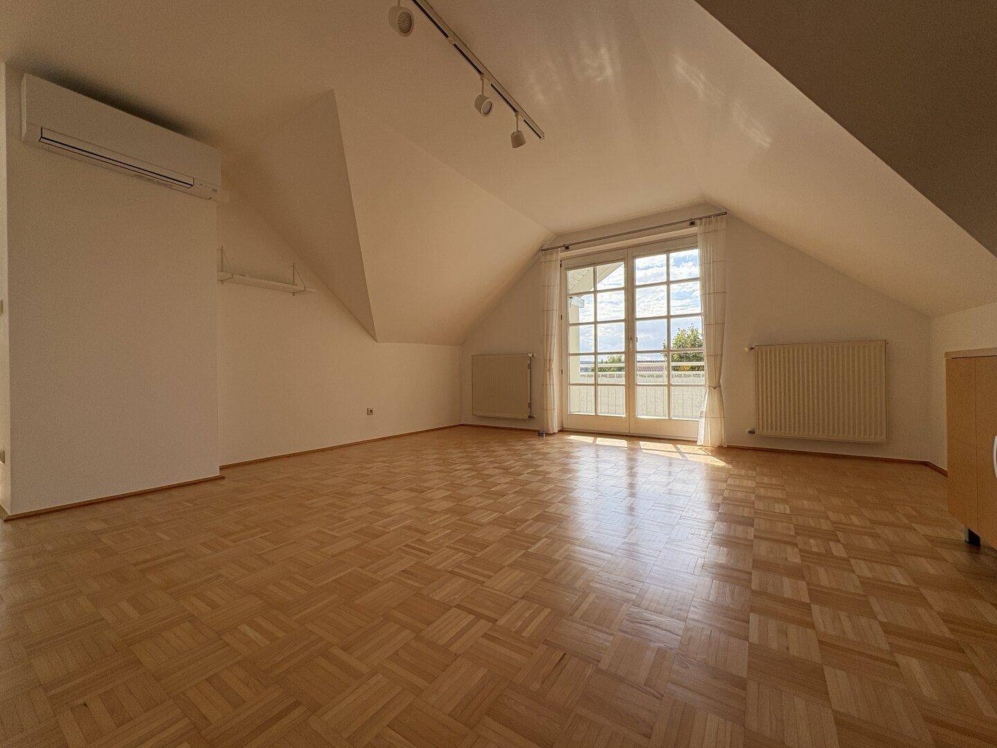 Lichtdurchflutetes Wohnzimmer mit Balkontür, Heizkörpern und schrägen Wänden.
