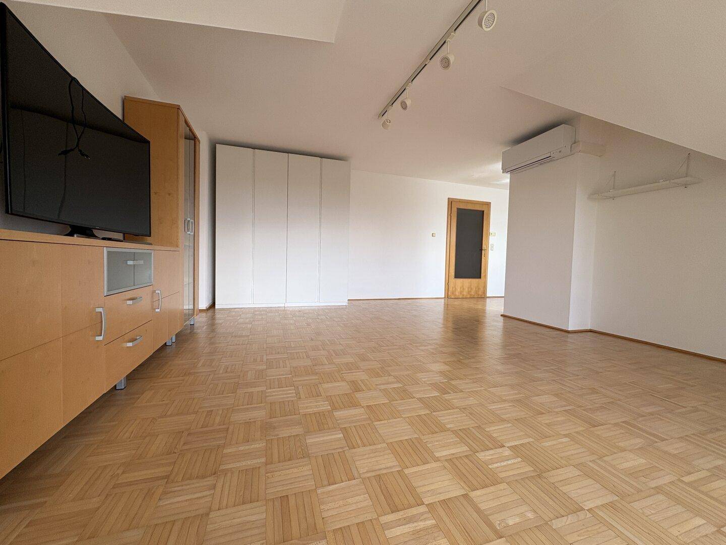Heller Wohnbereich mit Parkettboden, Einbauschrank und Klimaanlage im Dachgeschoss.