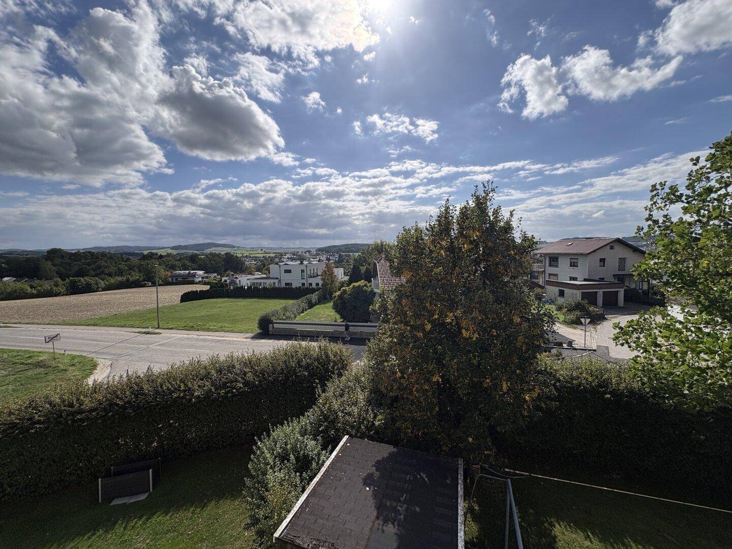 Weitläufiger Blick vom Balkon über die grüne Landschaft und umliegende Häuser.