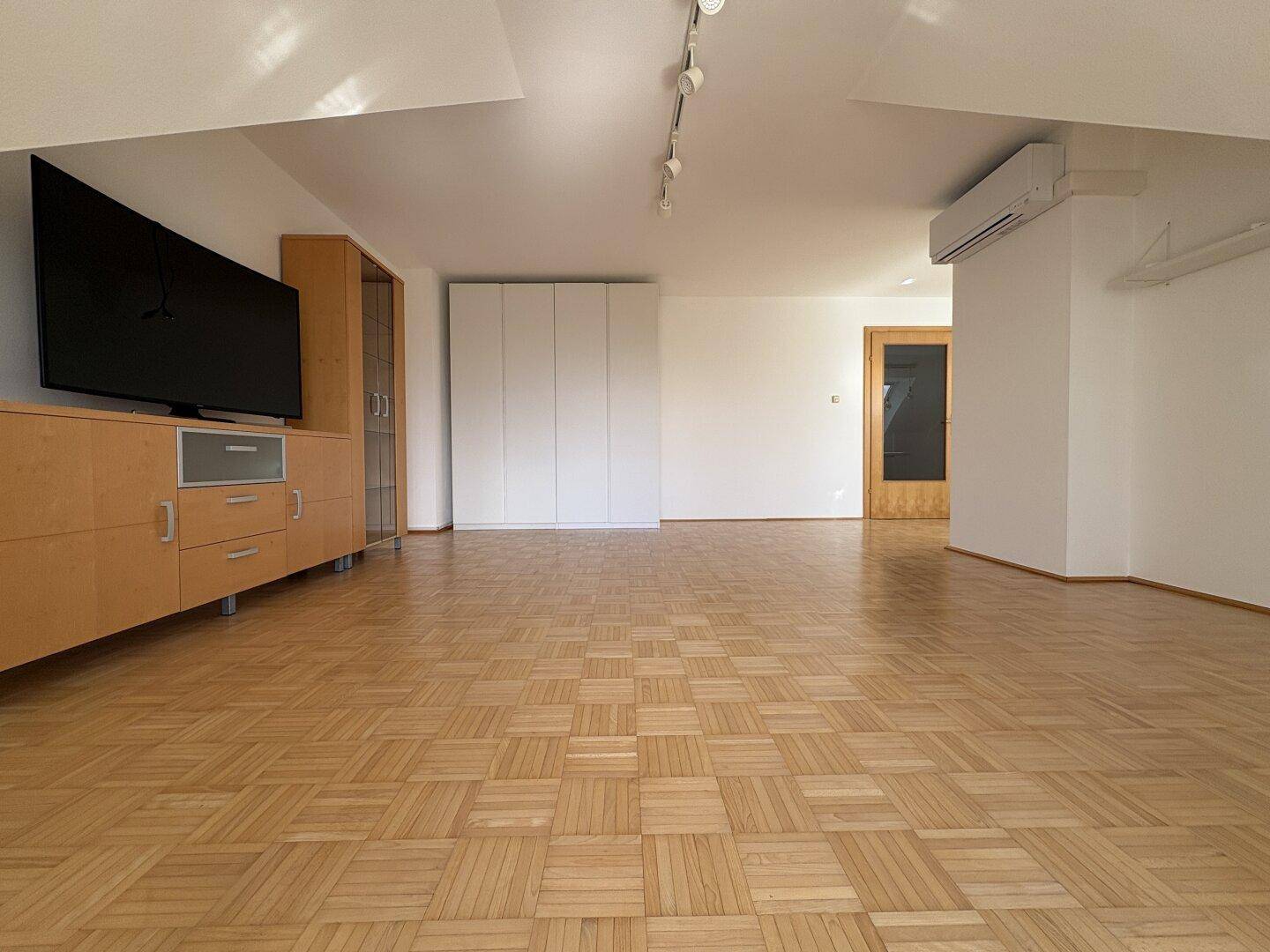 Großer Wohnbereich mit Parkettboden, Einbauschrank und Zugang zu weiteren Räumen.