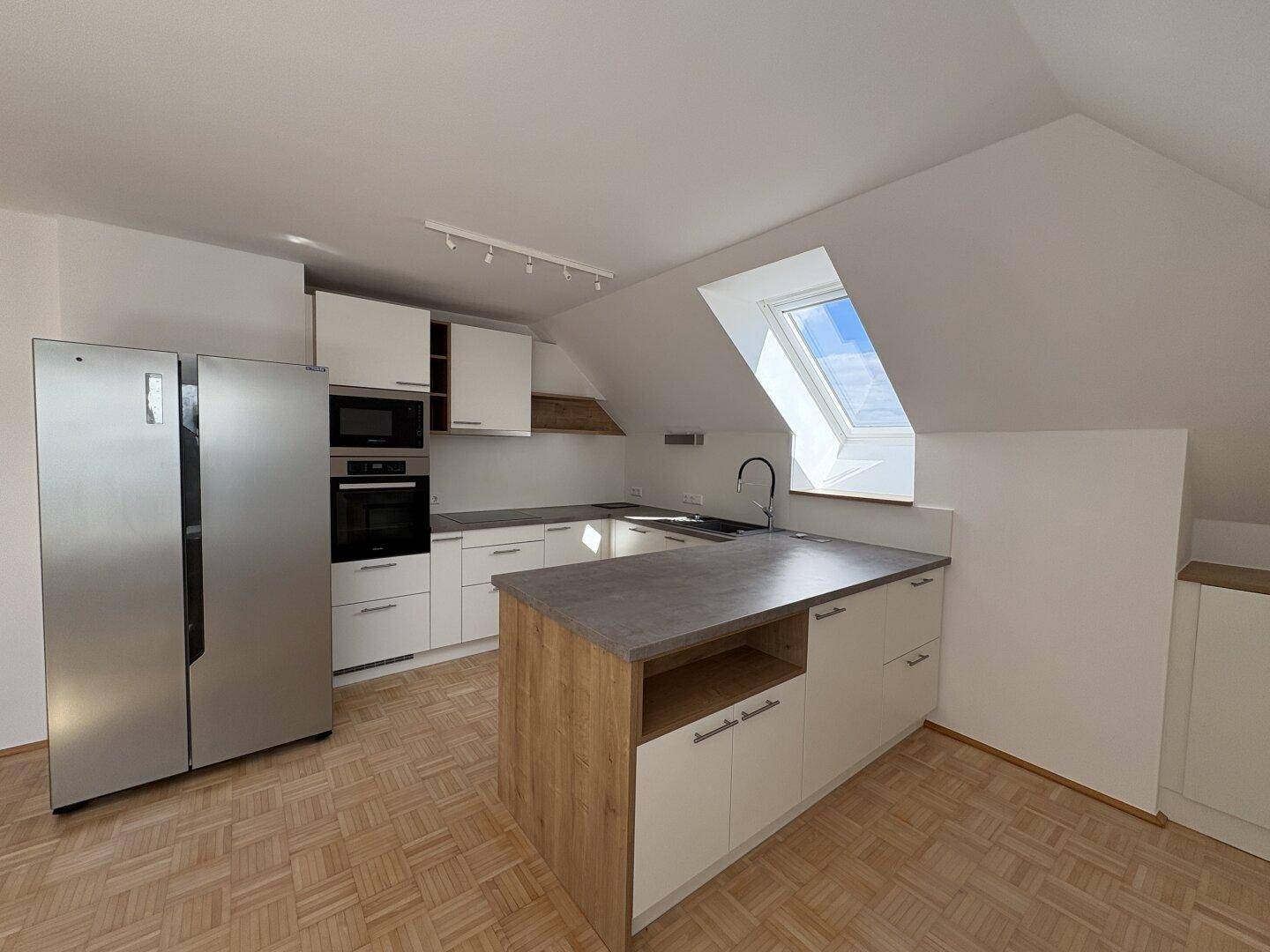 Gut ausgestattete Küche mit modernen Geräten, Kücheninsel und hellem Dachfenster.