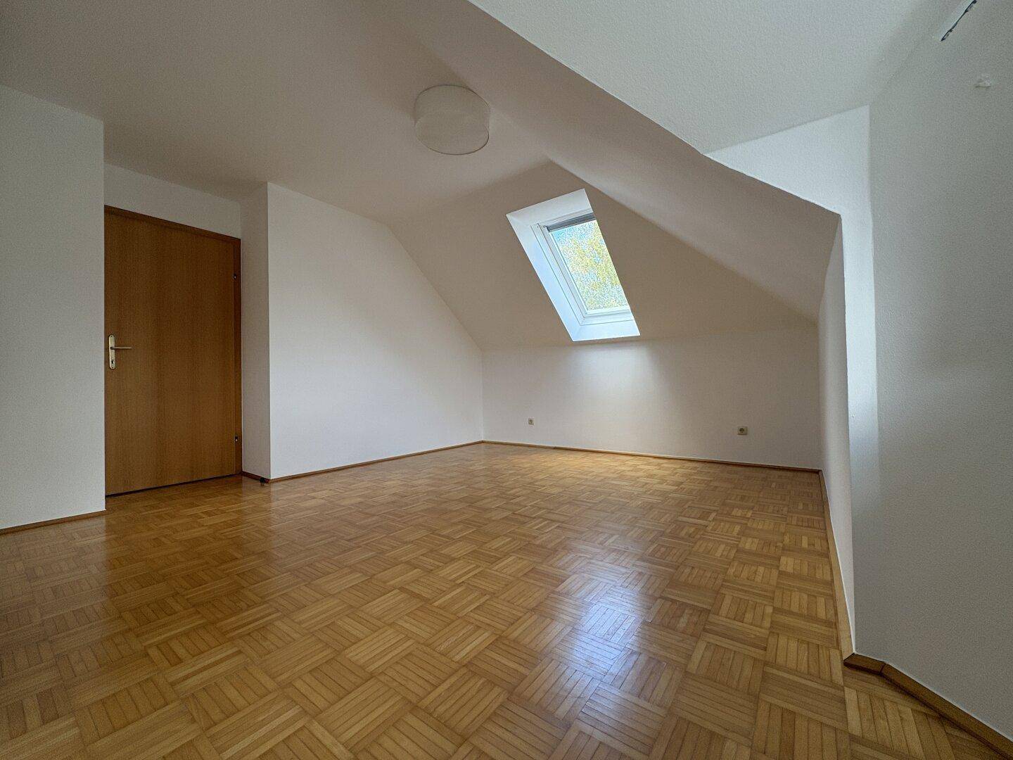 Lichtdurchflutetes Schlafzimmer mit Parkettboden, Dachfenster und Holztür.