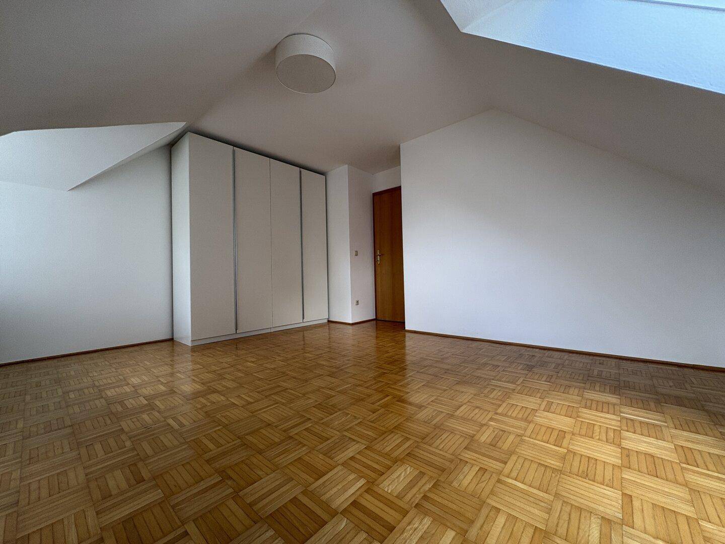 Großes Schlafzimmer mit Parkettboden, Einbauschrank und Dachschrägen.