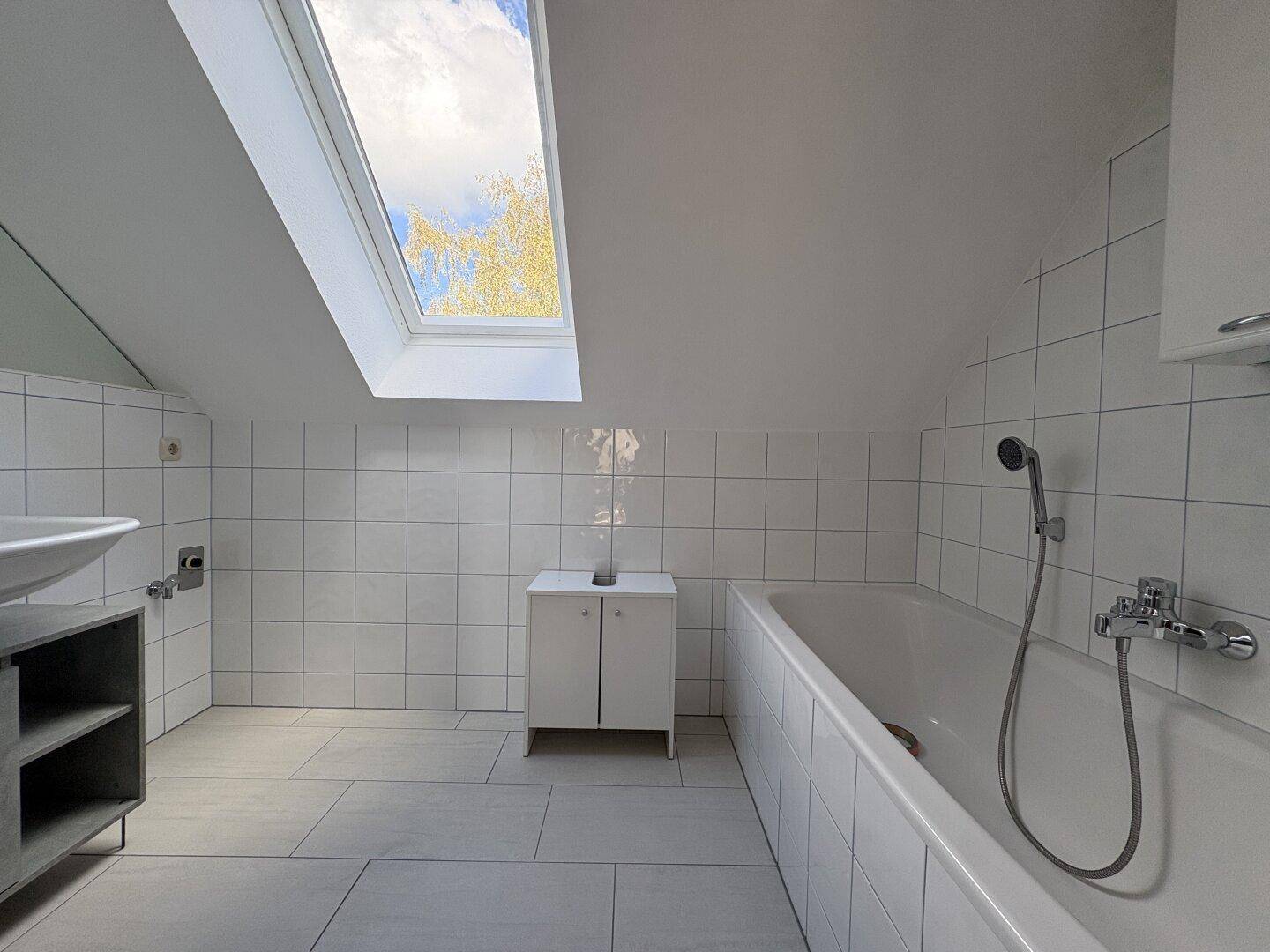 Helles Badezimmer mit Badewanne, Fliesenboden und Dachfenster.
