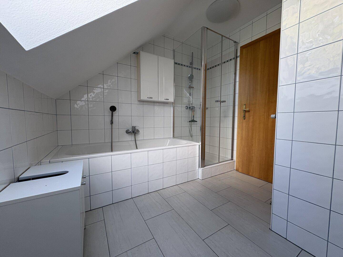 Badezimmer mit Badewanne, Duschkabine und weißen Fliesen im Dachgeschoss.