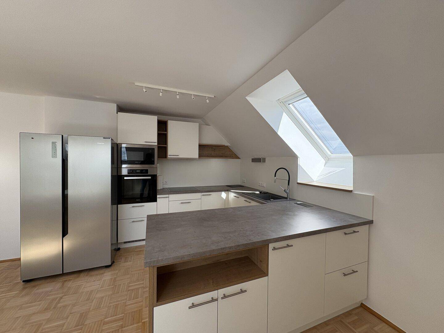 Moderne Einbauküche mit Edelstahlgeräten, Kücheninsel und Dachfenster für viel Tageslicht.
