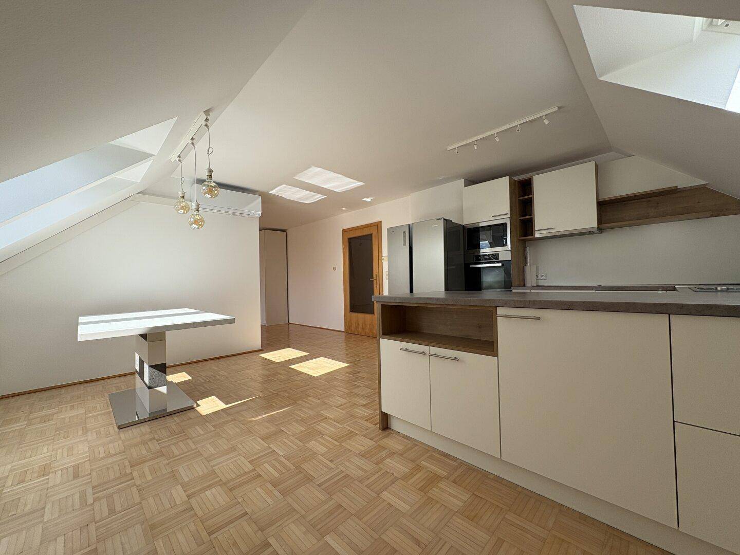 Offener Wohnbereich mit moderner Küche, Esstisch und viel Tageslicht durch Dachfenster.