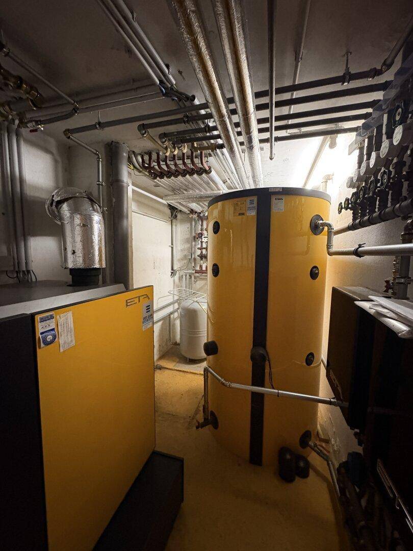 Heizungsraum mit großem Warmwasserspeicher und komplexer Rohrinstallation im Kellerbereich.