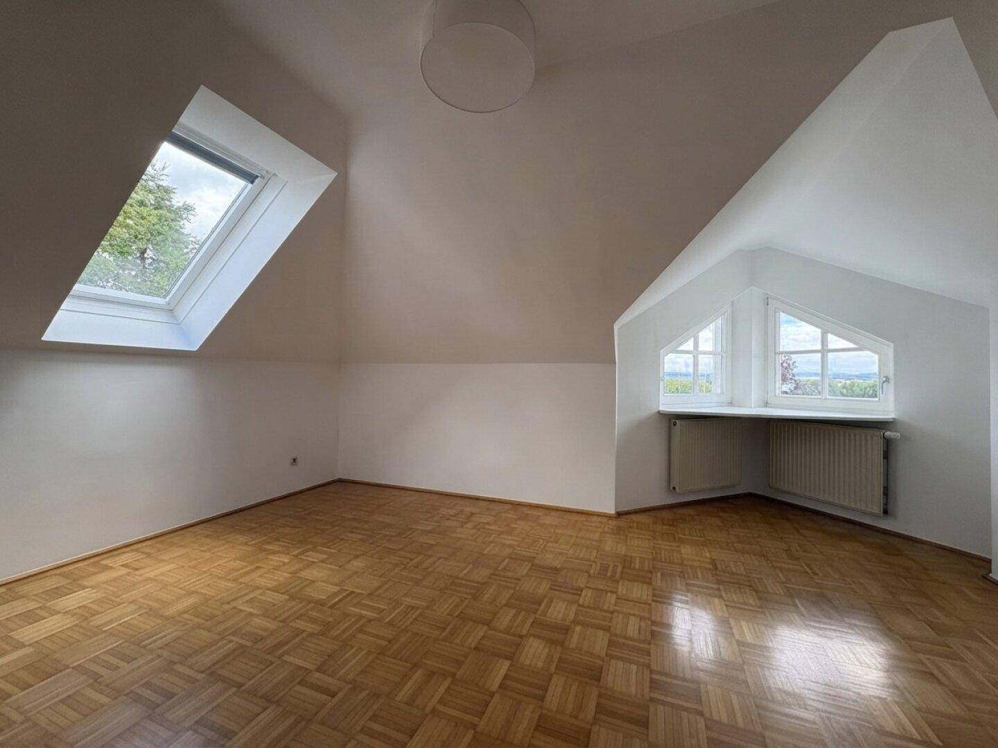 Helles Schlafzimmer mit Parkettboden, Dachfenstern und weitem Ausblick.