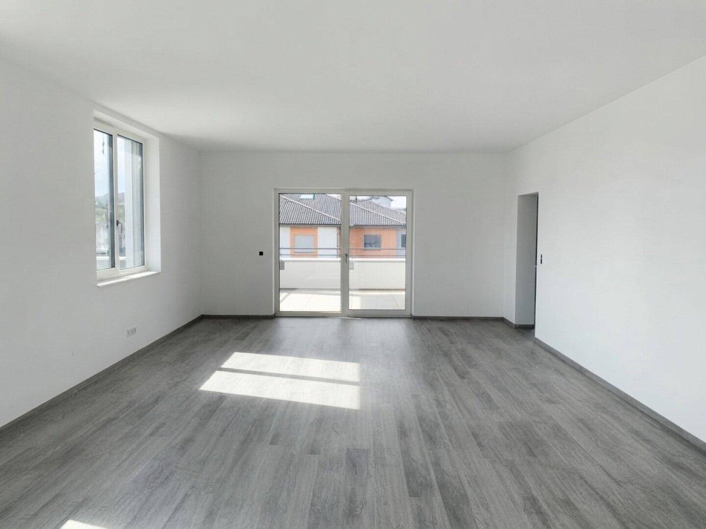 Geräumiger, heller Raum mit modernem Laminatboden und Zugang zu einem Balkon.