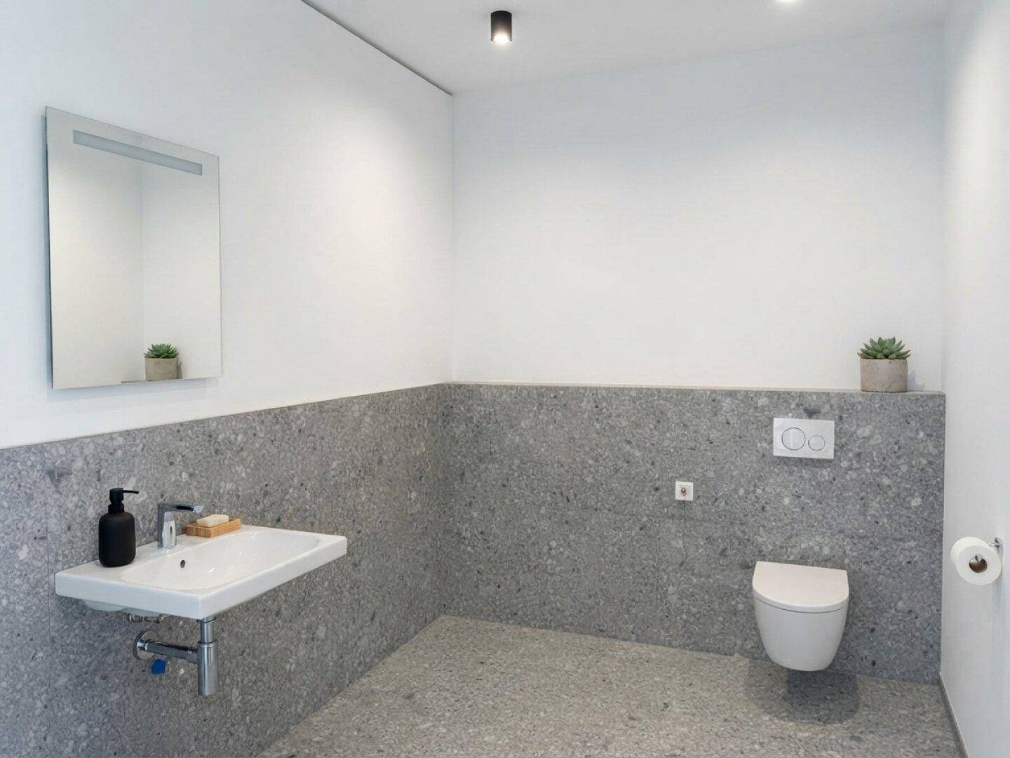 Modernes Badezimmer mit stilvollen grauen Fliesen, wandhängendem WC und Waschbecken.