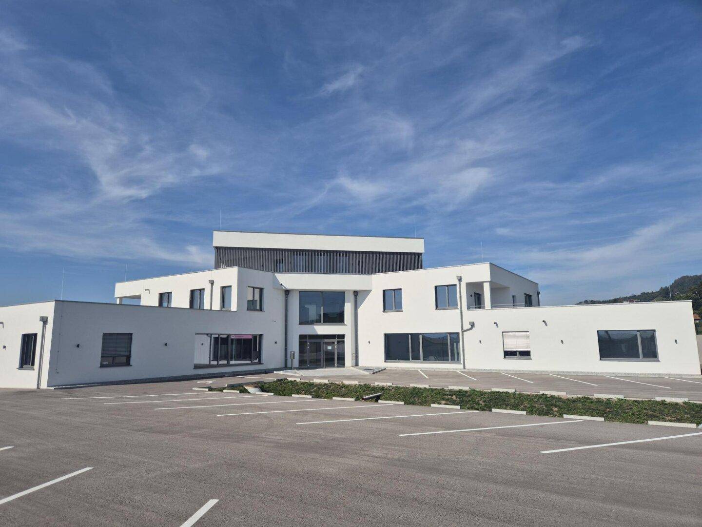 Ansicht des modernen Neubaus mit großem Parkplatz und minimalistischer Fassadengestaltung.