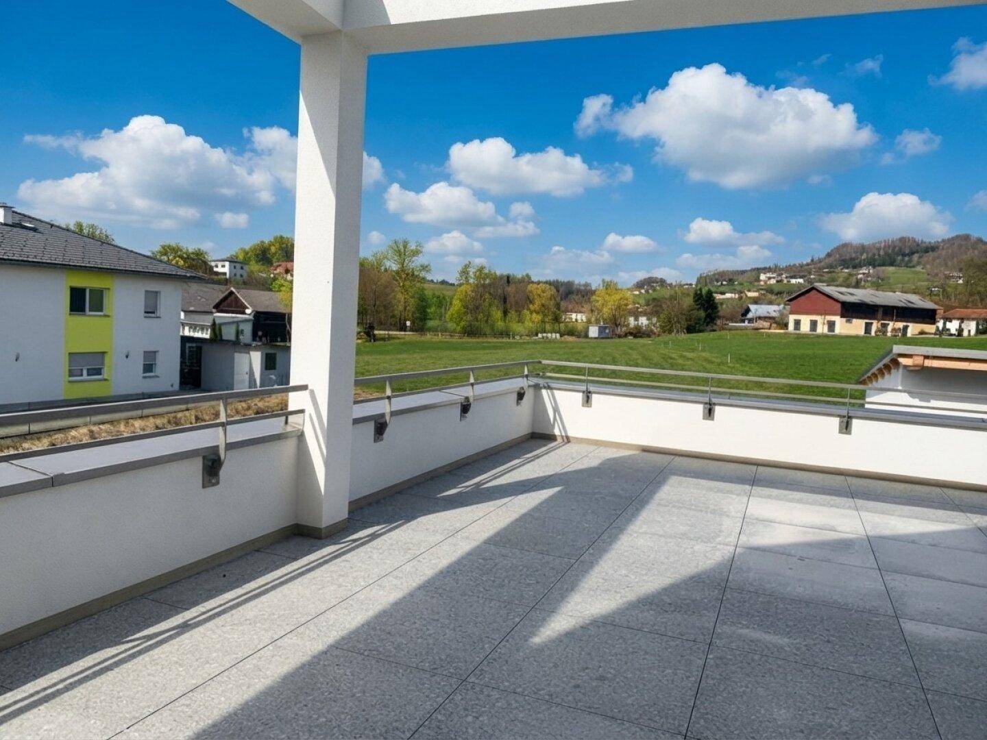 Helle Terrasse mit modernem Fliesenbelag und Panoramablick auf die ländliche Umgebung unter blauem Himmel.