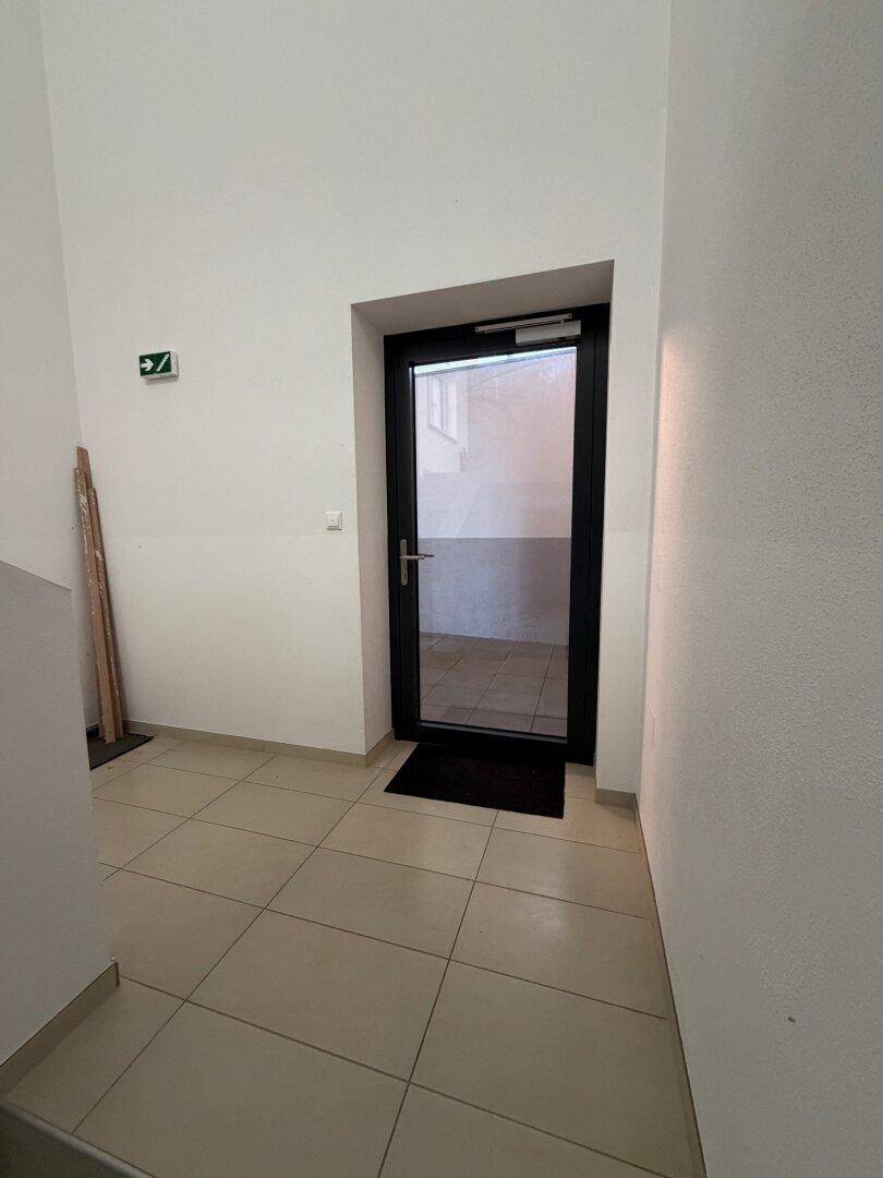 Heller Flur mit Fliesenboden und einer modernen schwarzen Glastür.