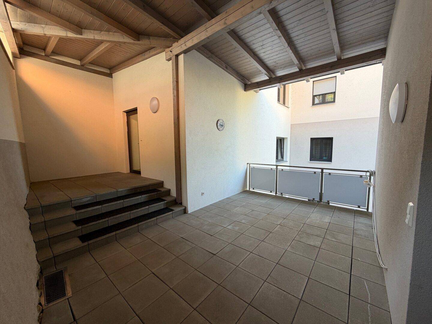 Überdachte Terrasse mit Fliesenboden, Holzdecke und einem Geländer, ideal für Entspannung im Freien.