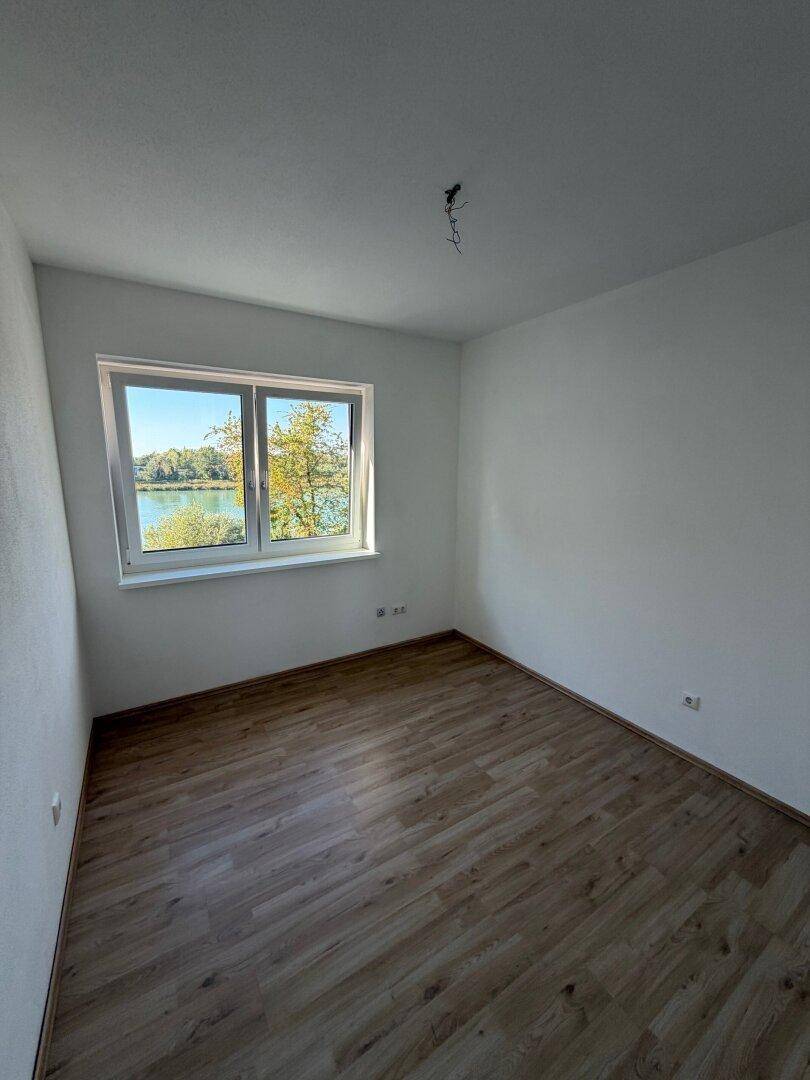 Schlafzimmer mit Laminatboden und einem Fenster, das einen schönen Blick auf den See und Bäume bietet.