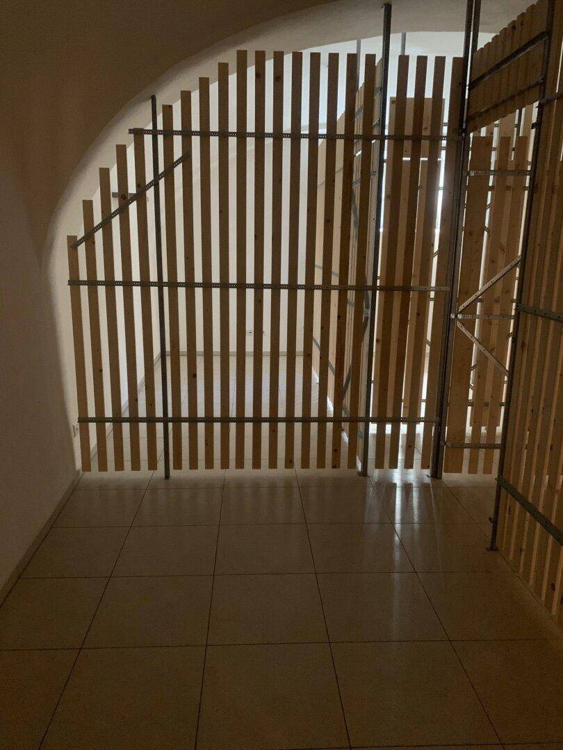 Lagerraum mit Fliesenboden und vertikalen Holzlatten als Abtrennungen, unter einer Gewölbedecke.