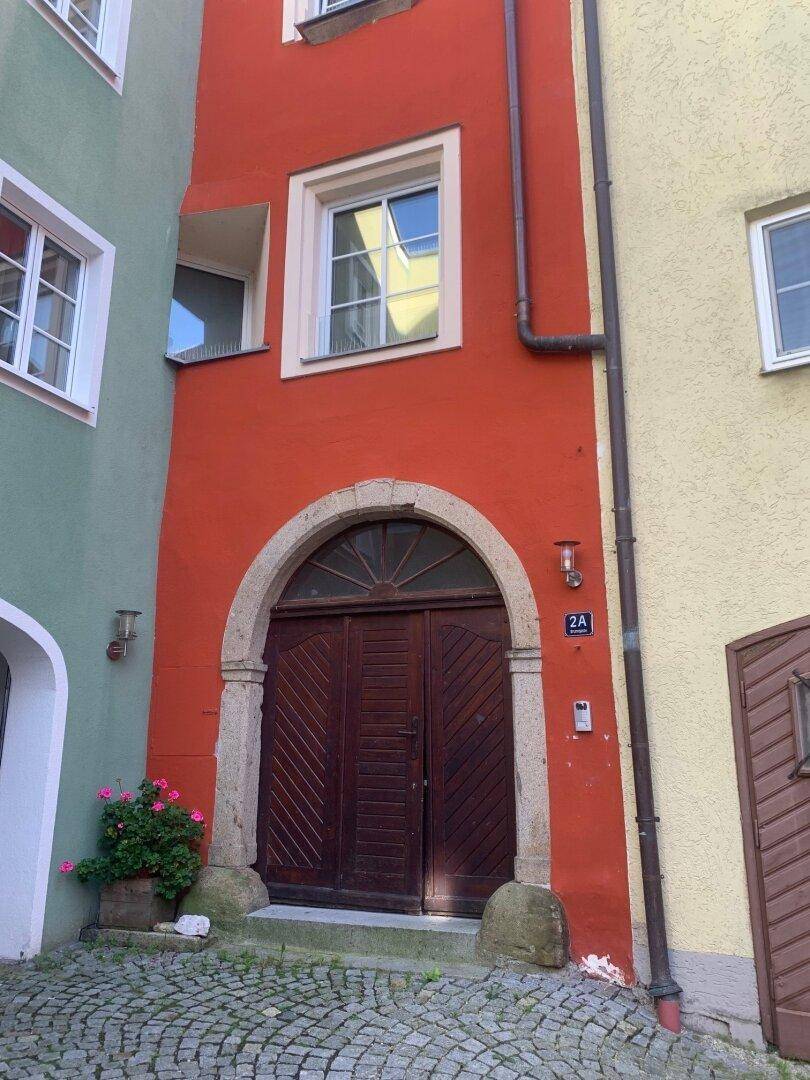 Historische Fassade eines Gebäudes in leuchtendem Rot mit einem großen Holztor und Kopfsteinpflaster.