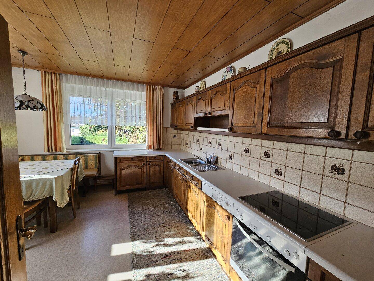Traditionelle Küche mit Holzdecke, Einbauküche und Essbereich am Fenster.