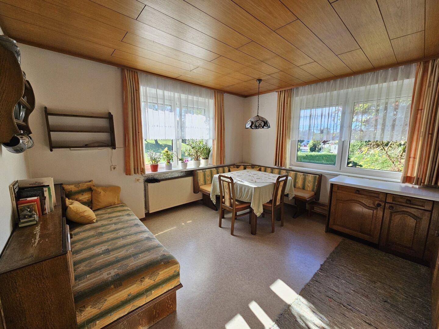 Gemütlicher Wohnbereich mit Holzdecke, Tagesbett und Esstisch am Fenster.