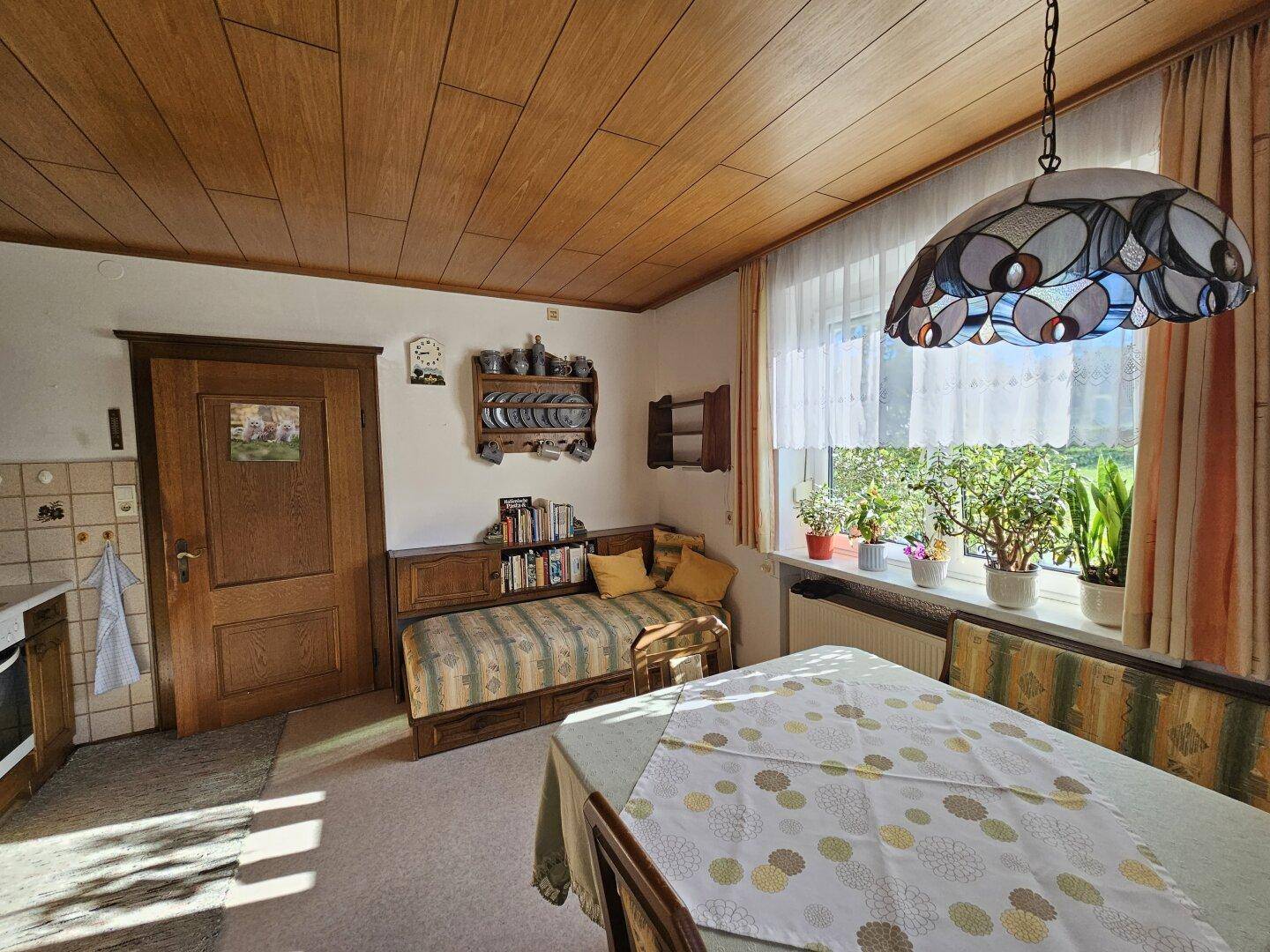 Heller Essbereich in der Küche mit Holzdecke, Tagesbett und Blick ins Grüne.