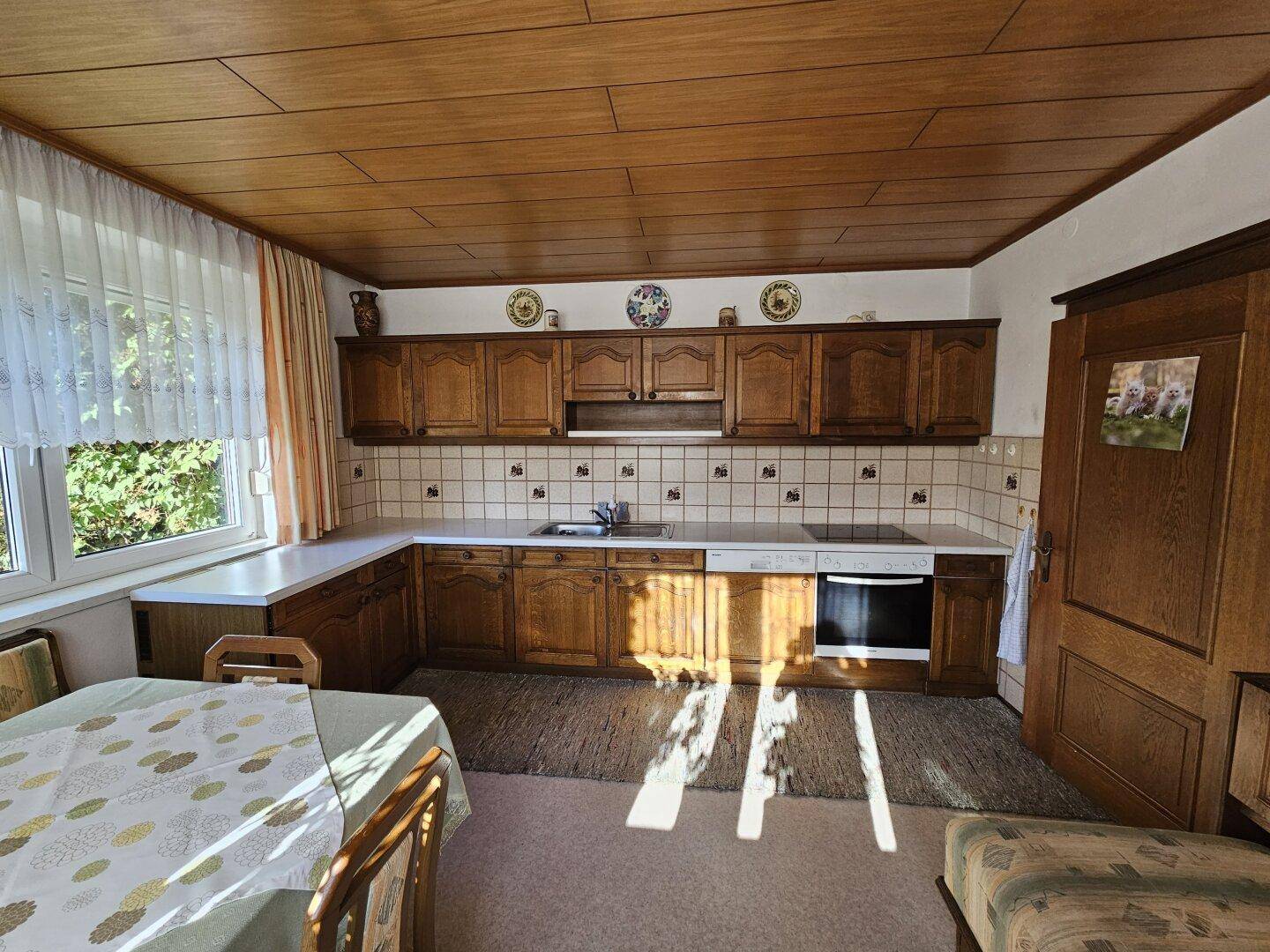 Geräumige Küche mit Holzschränken, Fliesenboden und Essbereich am Fenster.