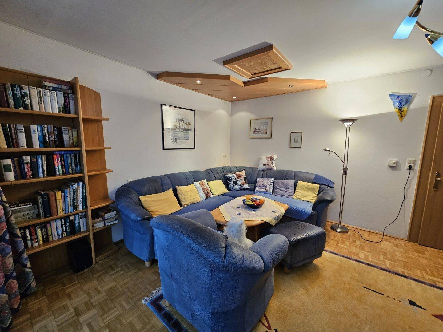 Gemütliches Wohnzimmer mit blauer Eckcouch, Bücherregal und Parkettboden.