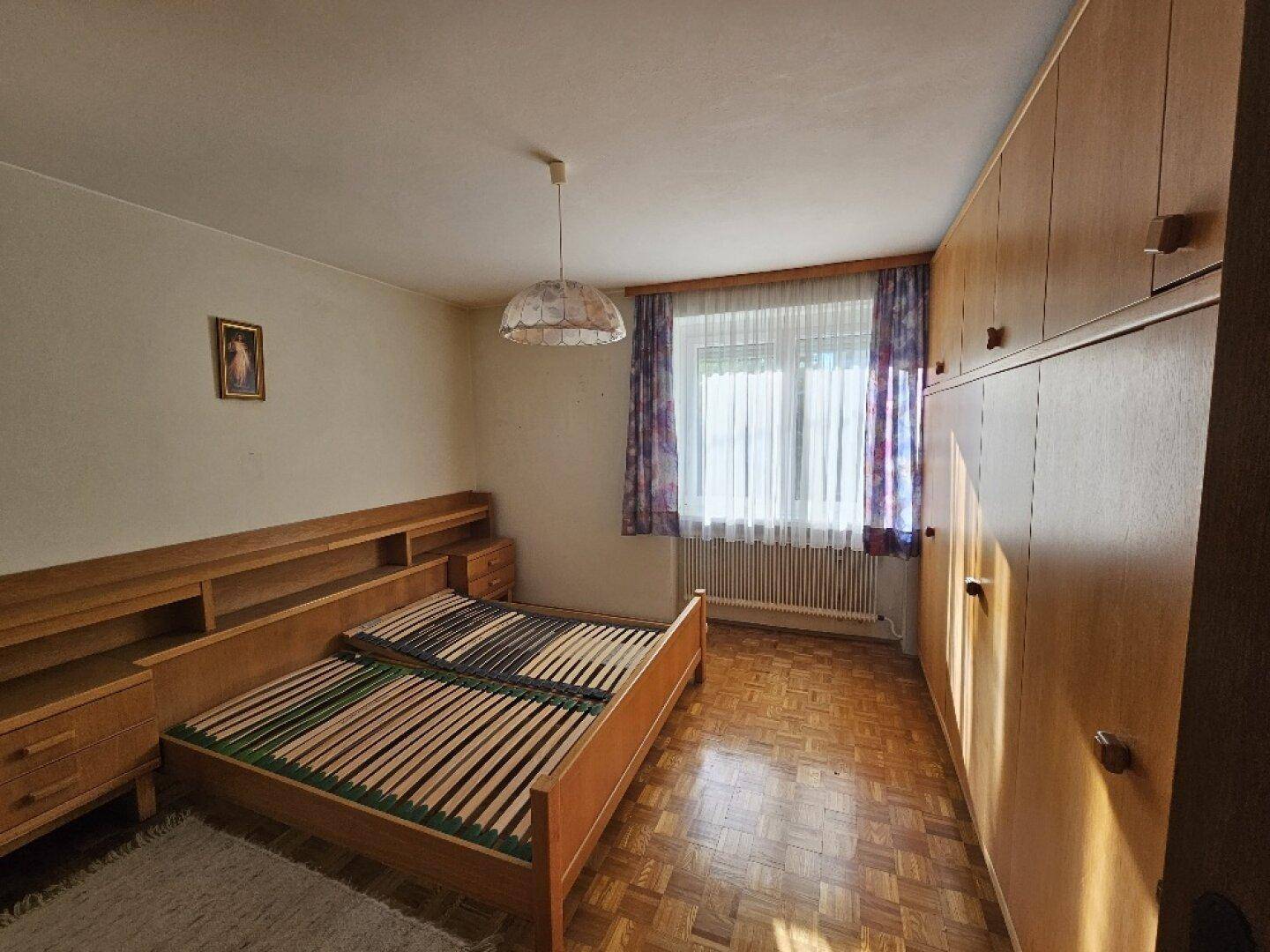 Helles Schlafzimmer mit großem Kleiderschrank, Doppelbett und Parkettboden.