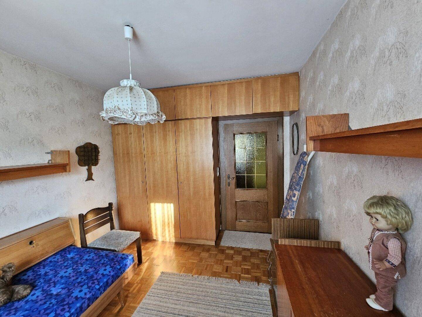 Helles Zimmer mit Einbauschränken, Einzelbett und Holzmöbeln.