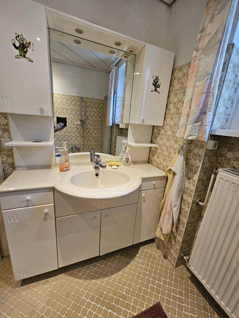 Badezimmer mit großem Spiegelschrank, Waschbecken und Fliesen im Retro-Stil.