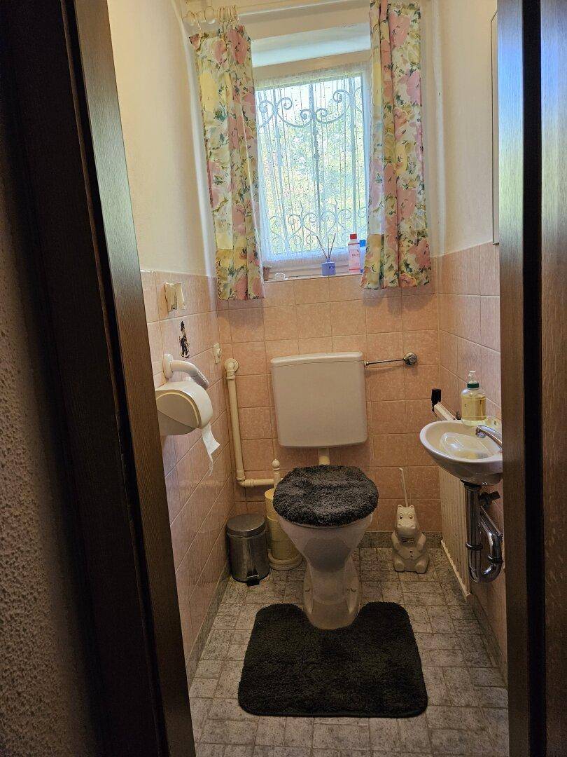 Kleines Gäste-WC mit Toilette, Waschbecken und Fenster.