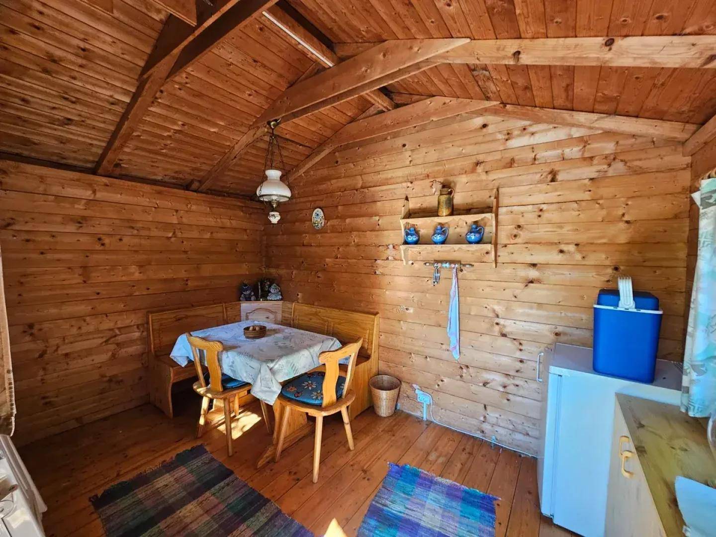 Gemütlicher Innenraum des Gartenhauses mit Holzwänden, Esstisch und kleiner Küchenzeile.