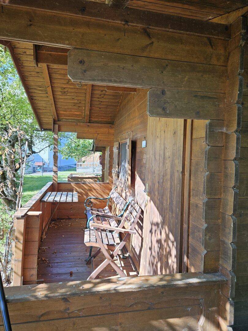 Überdachte Holzterrasse mit Sitzbänken am Gartenhaus, ideal zum Entspannen.