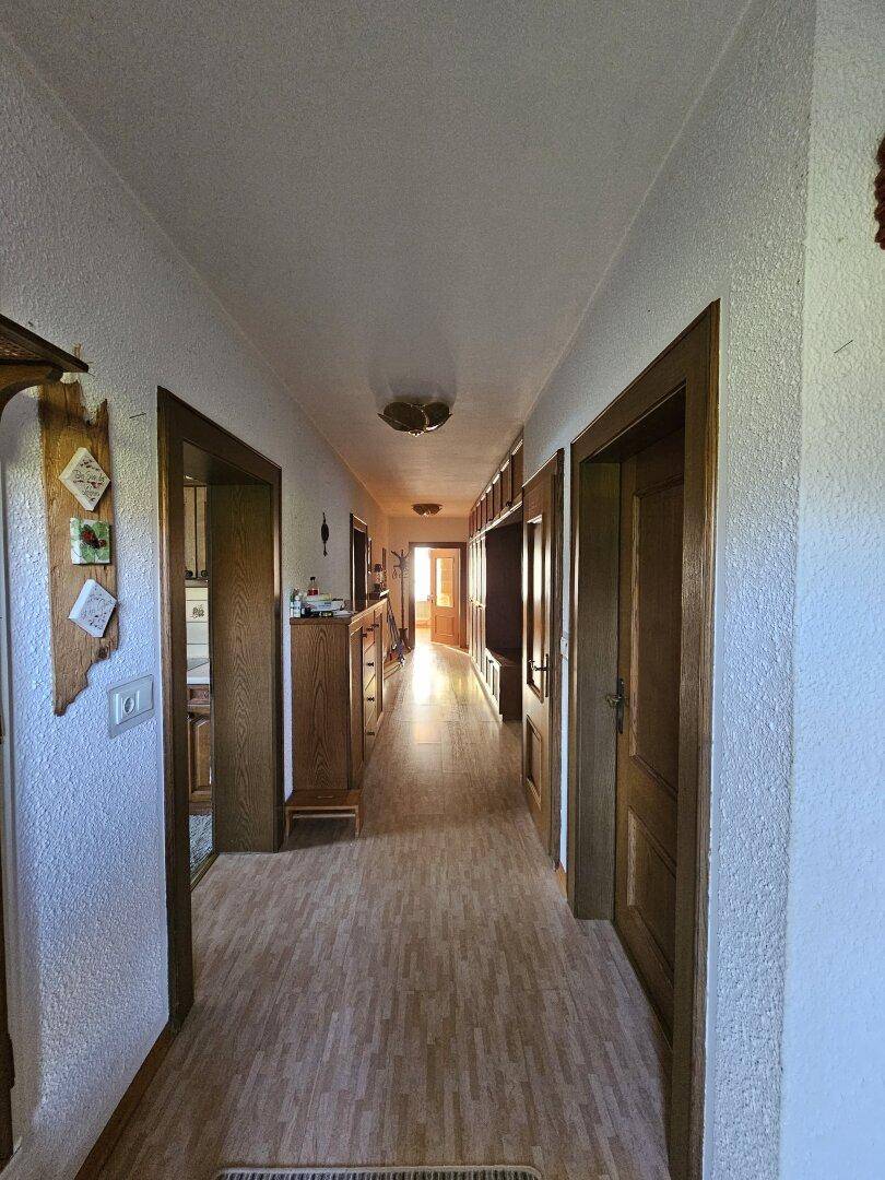 Langer Flur mit Laminatboden, Holztüren und strukturierten weißen Wänden, der viel natürliches Licht erhält.